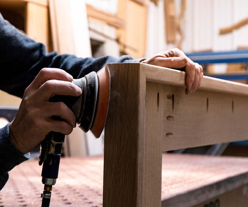 Why Americans Are Buying Amish-Made Furniture 1 Woodworker sanding a solid wood table leg in a furniture workshop
