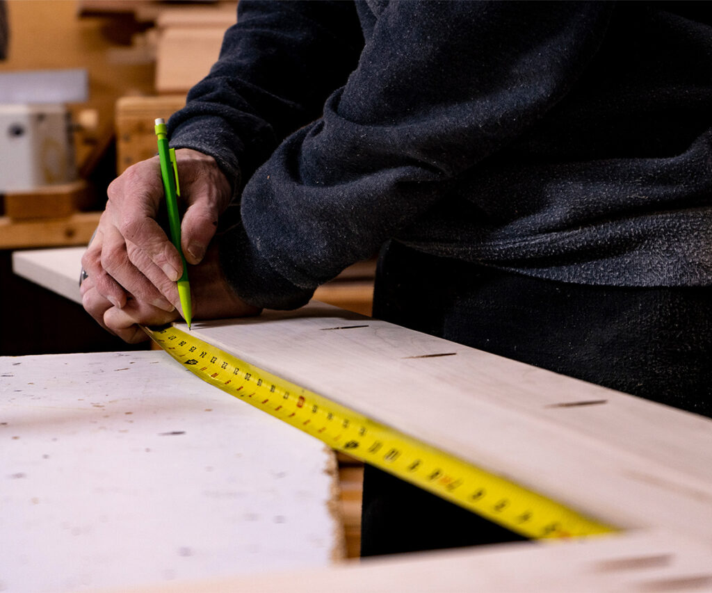 Why Americans Are Buying Amish-Made Furniture 9 Craftsman measuring a wood furniture part in an Amish workshop
