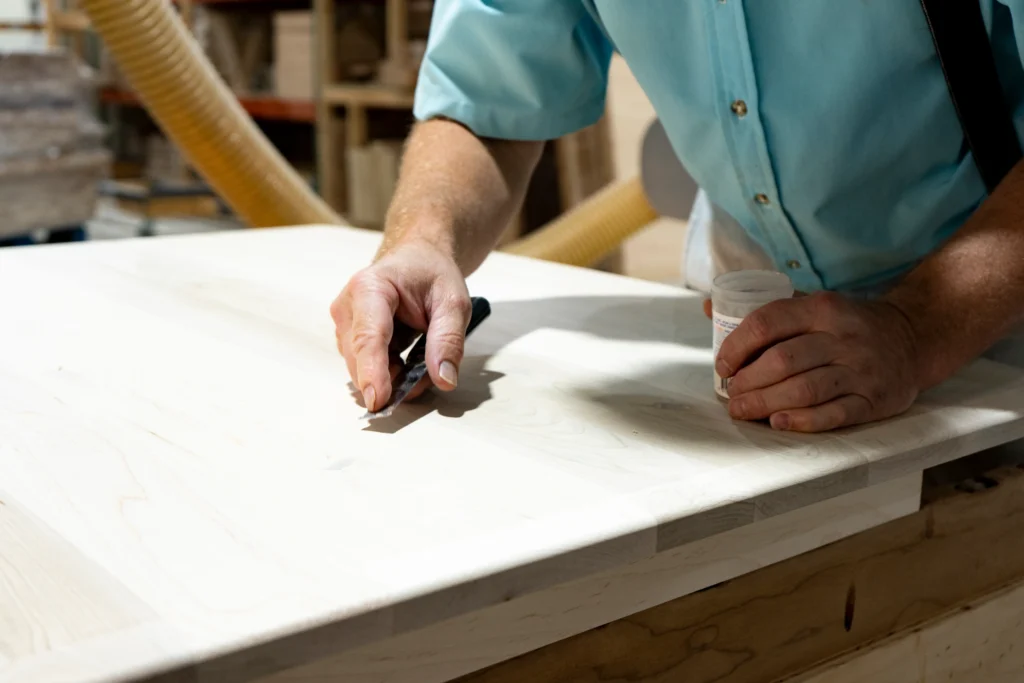 Craftsman hand-finishing a solid wood tabletop in a woodworking shop, illustrating the craftsmanship behind amish furniture cost.