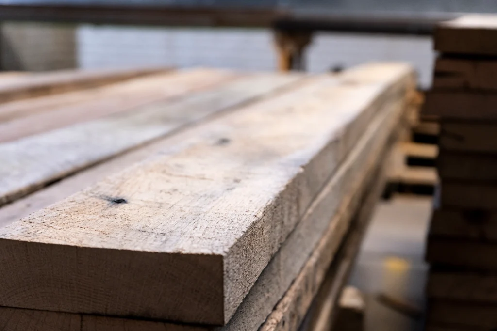 Rough-sawn solid wood boards stacked in a furniture workshop, showing natural grain and unfinished texture.